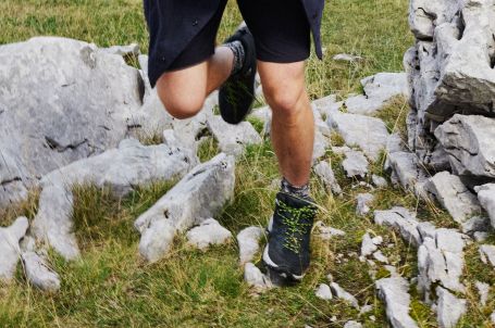 Nahaufnahme von Beinen mit Wanderschuhen auf einem felsigen Weg.